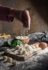Erntehelfer gießen Mehl auf rohe Gnocchi auf Holzbretter auf dem Tisch — Stockfoto