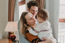 Happy parents and little child embracing at window at home. — Stock Photo