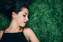 Mulher morena com lábios vermelhos deitado na grama e olhando para o lado — Fotografia de Stock