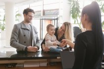 Staff worker at hotel reception giving key to family — Stock Photo