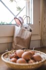 Bonito coelho branco sentado em saco de papel na cesta com ovos . — Fotografia de Stock