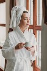 Задумчивая женщина пьет кофе после ванны и смотрит в камеру — стоковое фото