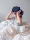 Веселый мальчик играет с VR очками на кровати — стоковое фото