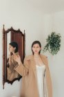 Стильна жінка в пальто стоїть біля дзеркала і вказує геть — стокове фото