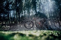 Side view of cyclist jumping on mountain bike at forest and splashes water — Stock Photo