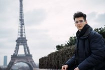 Jeune homme aux lunettes élégantes sur fond de tour Eiffel . — Photo de stock
