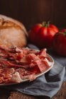 Spanish ham with tomatoes by loaf of bread on canvas — Stock Photo