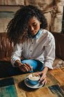 Гарненька молода жінка перемішує чашку кави за столом . — стокове фото