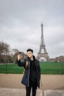 Young tourist man standing with phone and taking selfie on background of Eiffel tower. — Stock Photo