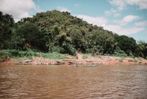 Small boats sailing in dirty water at hill covered with jungle forest. — Stock Photo