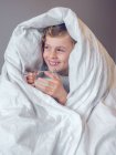 Хлопчик загорнутий у ковдру зі склянкою молока — стокове фото