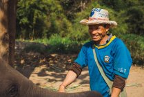 CHIANG RAI, THAILAND- FEBRUARY 12, 2018: Cheerful man standing in nature and stroking baby elephant. — Stock Photo