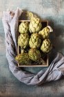 Raw artichokes in wooden box on stone table — Stock Photo