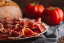 Still life of ham with tomatoes by bread on table — Stock Photo