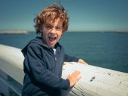Веселий хлопчик на поручнях над мальовничим морем — стокове фото