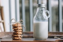 Botella de leche y galletas en mesa de madera . - foto de stock