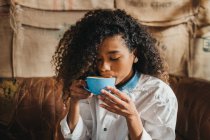 Lockige junge Frau trinkt eine Tasse Kaffee — Stockfoto