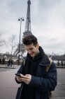 Lächelnder junger Mann, der auf dem Hintergrund des Eiffelturms steht und mit dem Smartphone spricht. — Stockfoto