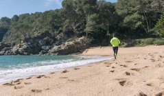 Vista trasera del hombre corriendo a lo largo de la playa de arena - foto de stock