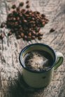 Taza de café por pila de granos de café en la mesa de madera - foto de stock