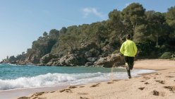 Visão traseira do homem correndo ao longo da praia idílica — Fotografia de Stock