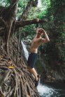 Fröhlicher akrobatischer Mann, der am Baum hängt und mit der Hand bis zum Kopf in die Kamera blickt. — Stockfoto
