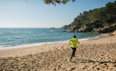 Visão traseira do homem correndo na praia de areia idílica — Fotografia de Stock