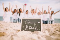 Blackboard with team bride lettering over unrecognizable women posing with hands up at  on beach. — Stock Photo