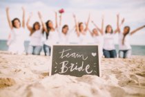 Tafel mit Teambraut-Schriftzug über unkenntlichen Frauen, die mit erhobenen Händen am Strand posieren. — Stockfoto