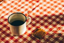 White metal cup with coffee on checkered tablecloth with cookies. — Stock Photo