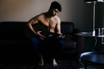 Homem sem camisa com guitarra em casa — Fotografia de Stock