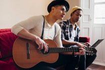Young stylish men resting on sofa with laptop ad guitar — Stock Photo