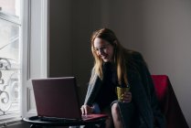 Mulher em poltrona de navegação laptop e beber café — Fotografia de Stock
