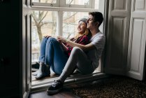 Seitenansicht eines jungen Paares, das sich auf der Fensterbank umarmt — Stockfoto