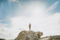 Jovem mulher de pé no penhasco contra o céu ensolarado — Fotografia de Stock