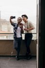 Amigos multiétnicos tomando selfie con teléfono inteligente en el balcón - foto de stock