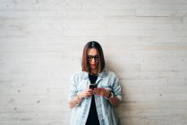 Brunette woman browsing smartphone at concrete wall — Stock Photo