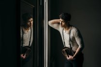 Мечтательный человек в винтажной одежде, опирающийся на стену и смотрящий в окно — стоковое фото