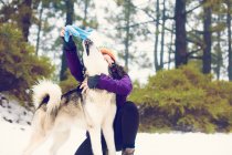 Donna ridente che gioca con il cane nei boschi invernali — Foto stock