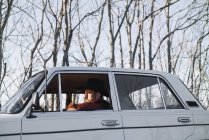 Бородатого мужчини в капелюсі водіння vintage білий автомобіль в природі. — стокове фото