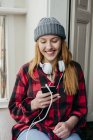Fröhliche blonde Frau mit Kopfhörern, die im Smartphone surft — Stockfoto