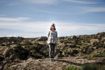 Jovem mulher em pé no penhasco contra a paisagem rochosa e céu — Fotografia de Stock