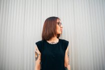 Stylische tätowierte Frau steht an Metallwand und schaut zur Seite — Stockfoto