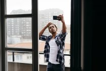 Stilvoller junger Mann steht auf Balkon und macht Selfie. — Stockfoto