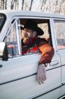 Bearded man in hat driving white car in nature. — Stock Photo