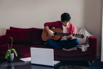 Young man playing guitar on coach at home — Stock Photo