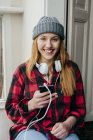 Smiling young blonde woman with headphones and smartphone and looking at camera. — Stock Photo