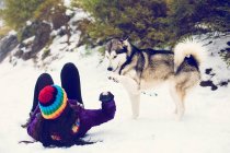 Жінка лежить на снігу і грає з собакою — стокове фото