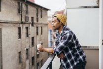 Stylish man in knitted hat drinking coffee on balcony — Stock Photo