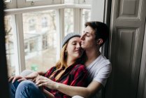 Sensual pareja abrazando con los ojos cerrados en ventana alféizar - foto de stock
